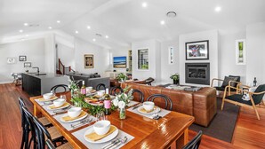A spacious living area with a dining table set for a meal, a fireplace, and a modern kitchen in the background. - Hunter Treehouse - Gorgeous golf course getaway, at The Vintage Resort (Rothbury)