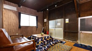 A room with a wooden floor, a brown leather sofa, a patterned sofa, a small table with a plant, and a window with a curtain. - Tokyo House (Tokyo)