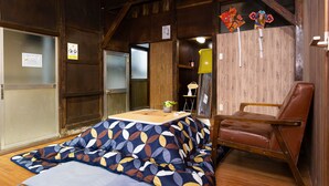 A room with a wooden ceiling, a sofa with a leaf-patterned cover, a brown leather chair, and a small table with a plant. - Tokyo House (Tokyo)