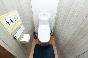 Ein schmales Badezimmer mit Holzvertäfelung, einer weißen Toilette, einem Handdesinfektionsmittelspender und einer kleinen Mülltonne.