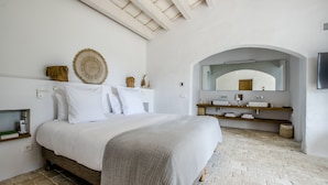 A bedroom with a large bed, a vanity with a mirror, and a brick floor.