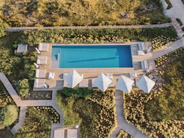 Vista aérea de una piscina rectangular rodeada de zonas de terraza de madera con sillas de salón y sombrillas.