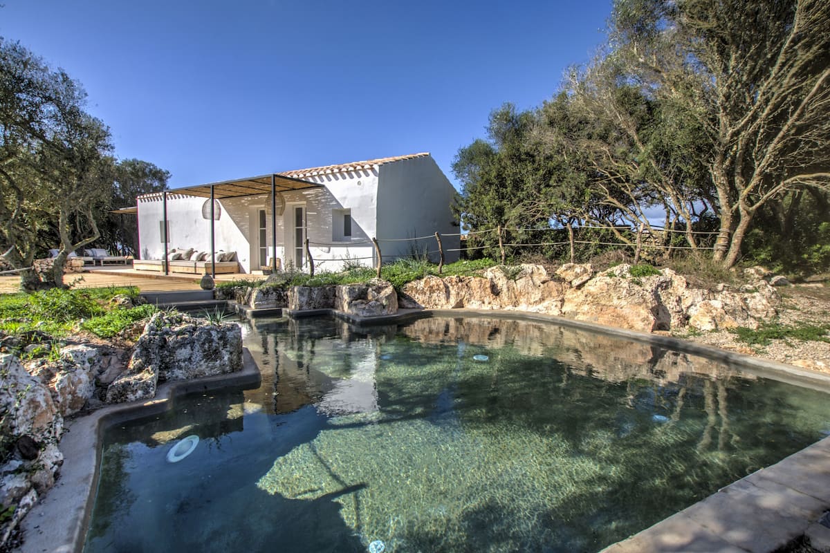 A modern villa with a swimming pool, surrounded by natural landscape and trees.