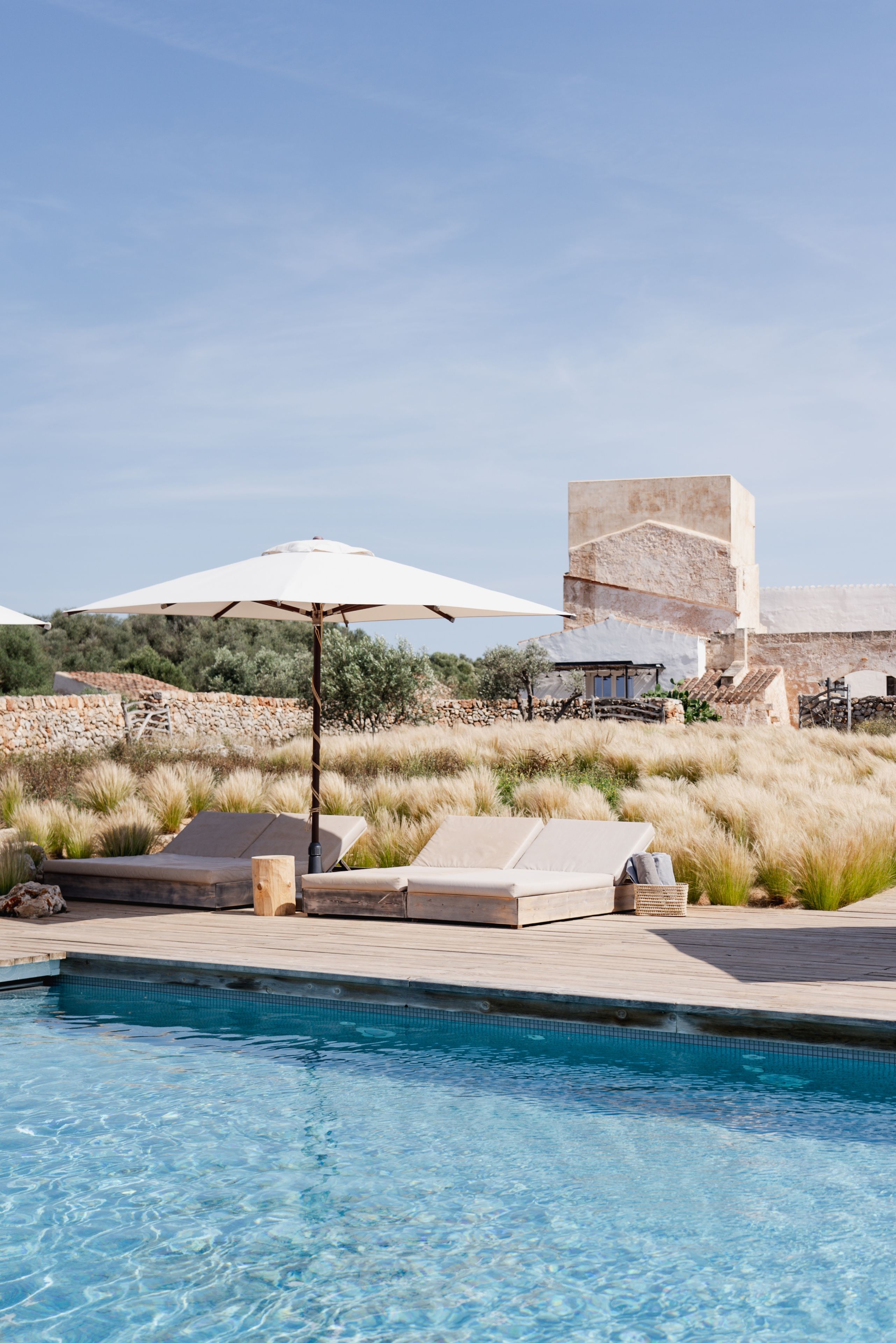 A pool area with lounge chairs, a white umbrella, and a stone building in the background.