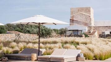 A pool area with lounge chairs, a white umbrella, and a stone building in the background.