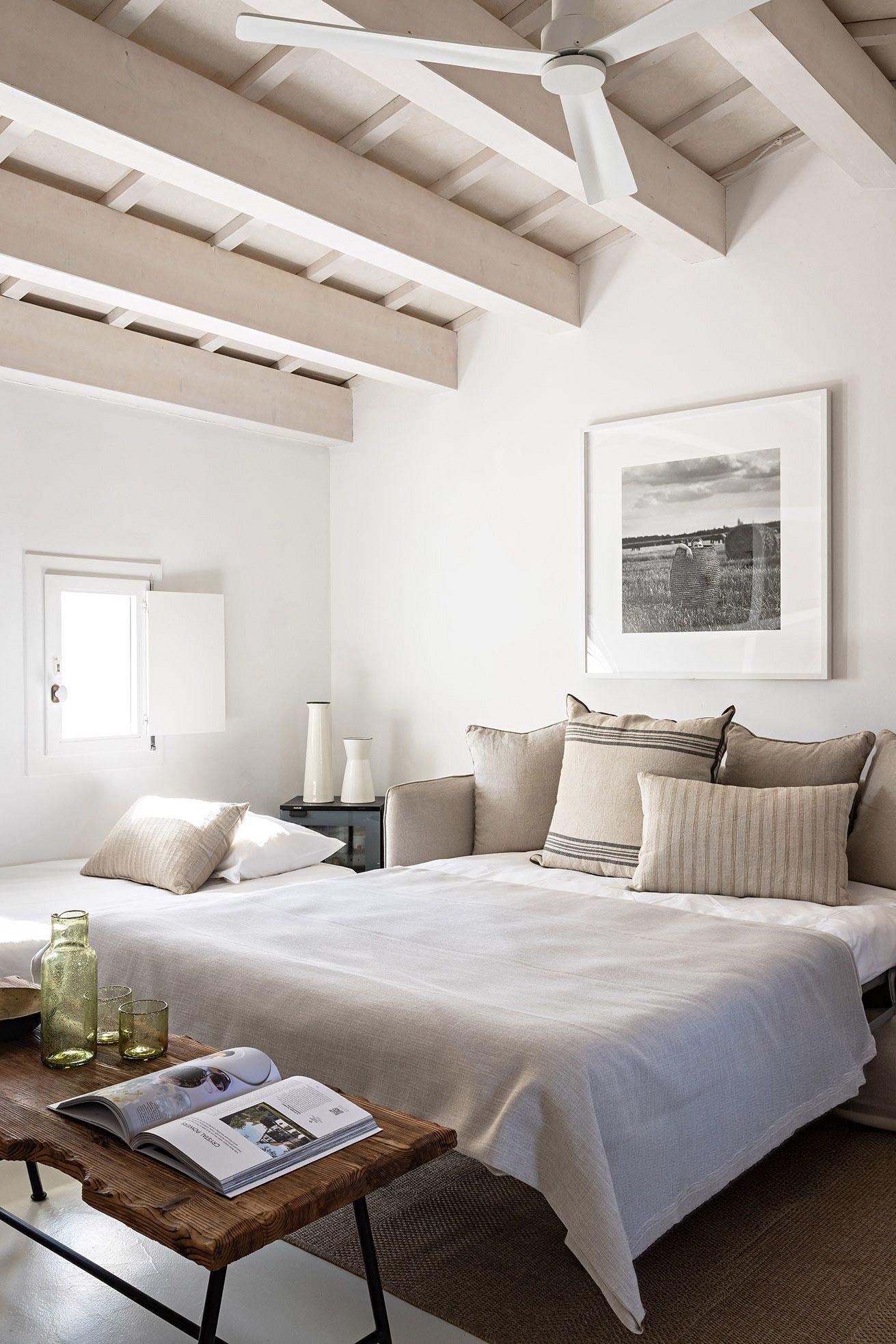 A bedroom with a large bed, a ceiling fan, a framed picture, bedside tables, and a window.