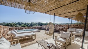 An outdoor lounge area with a pool, wicker furniture, and a stone wall backdrop. - Torre Vella – Fontenille Collection (Alayor)