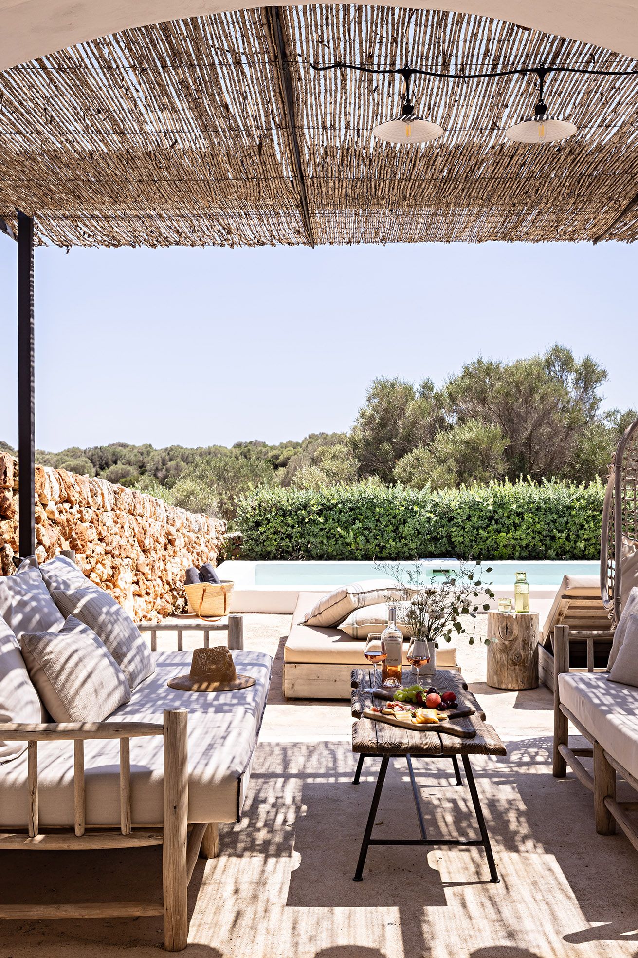 An outdoor seating area with a pool view, furnished with sofas and a table with food and drinks.