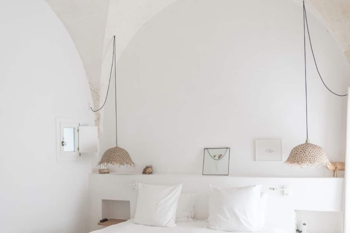 A minimalist bedroom with a large bed, two pendant lights, and a small bedside table.