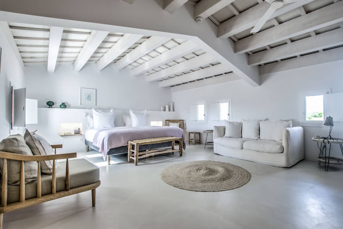 A spacious living room with a large bed, a white sofa, and a wooden bench.