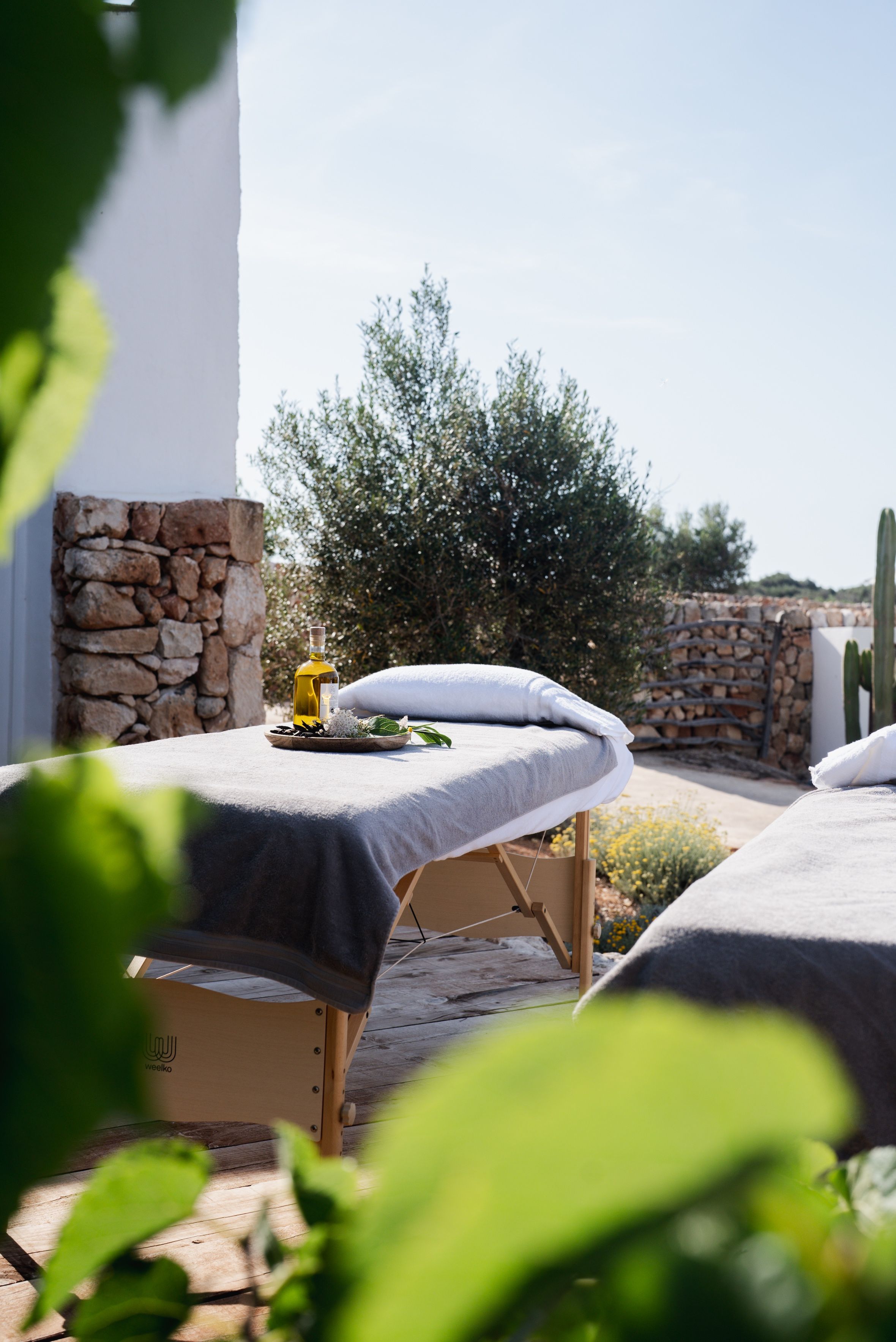 A spa area with two massage tables, a bottle of oil, and a bowl of flowers.