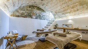 A spa room with wooden floors, a stone arch ceiling, and a massage table with towels. - Torre Vella – Fontenille Collection (Alayor)