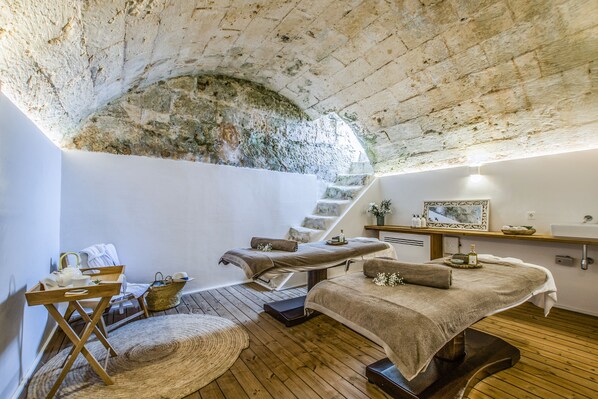 A spa room with wooden floors, a stone arch ceiling, and a massage table with towels. - Torre Vella – Fontenille Collection (Alayor)