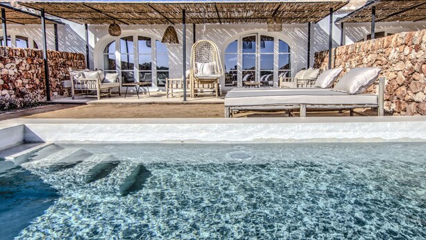 A poolside area with a stone wall, lounge chairs, and a hanging chair. - Torre Vella – Fontenille Collection (Alayor)