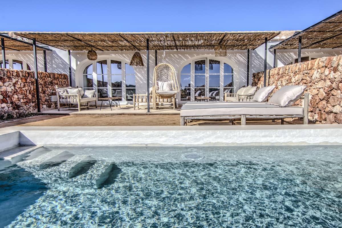 A poolside area with a stone wall, lounge chairs, and a hanging chair.