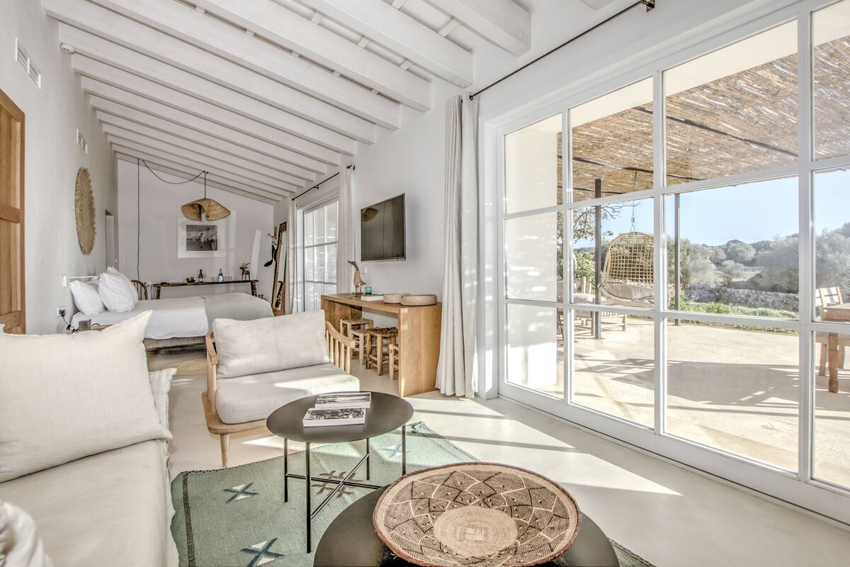 A spacious room with a large window, a wooden ceiling, a sofa, a dining area, and a bed.