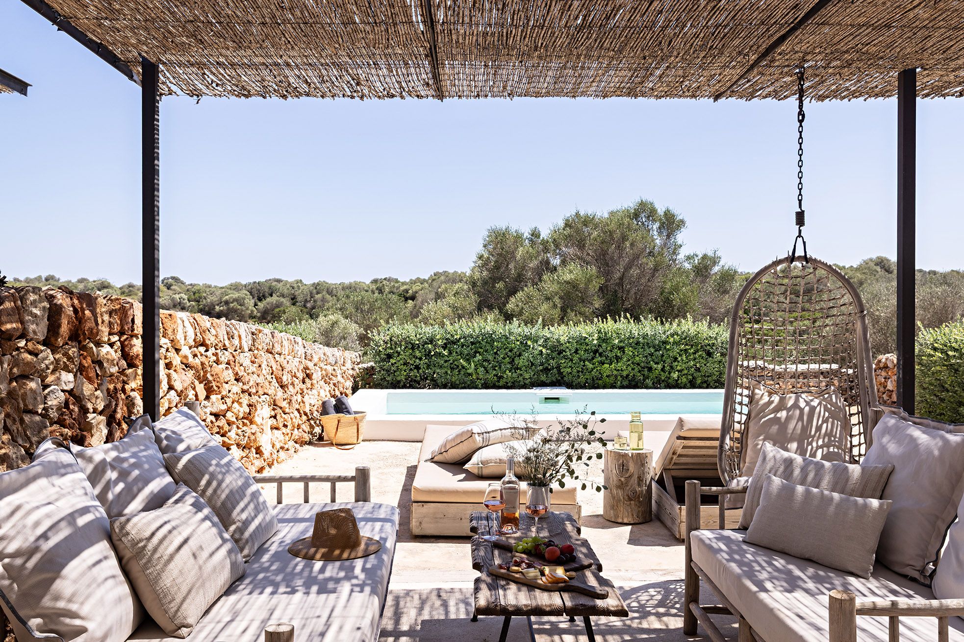 A covered outdoor seating area with a pool in the background.