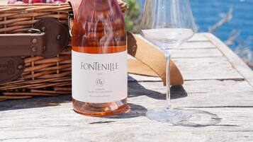 Una botella de vino, una copa, una cesta de mimbre con uvas sobre una mesa de madera con vista al mar.
