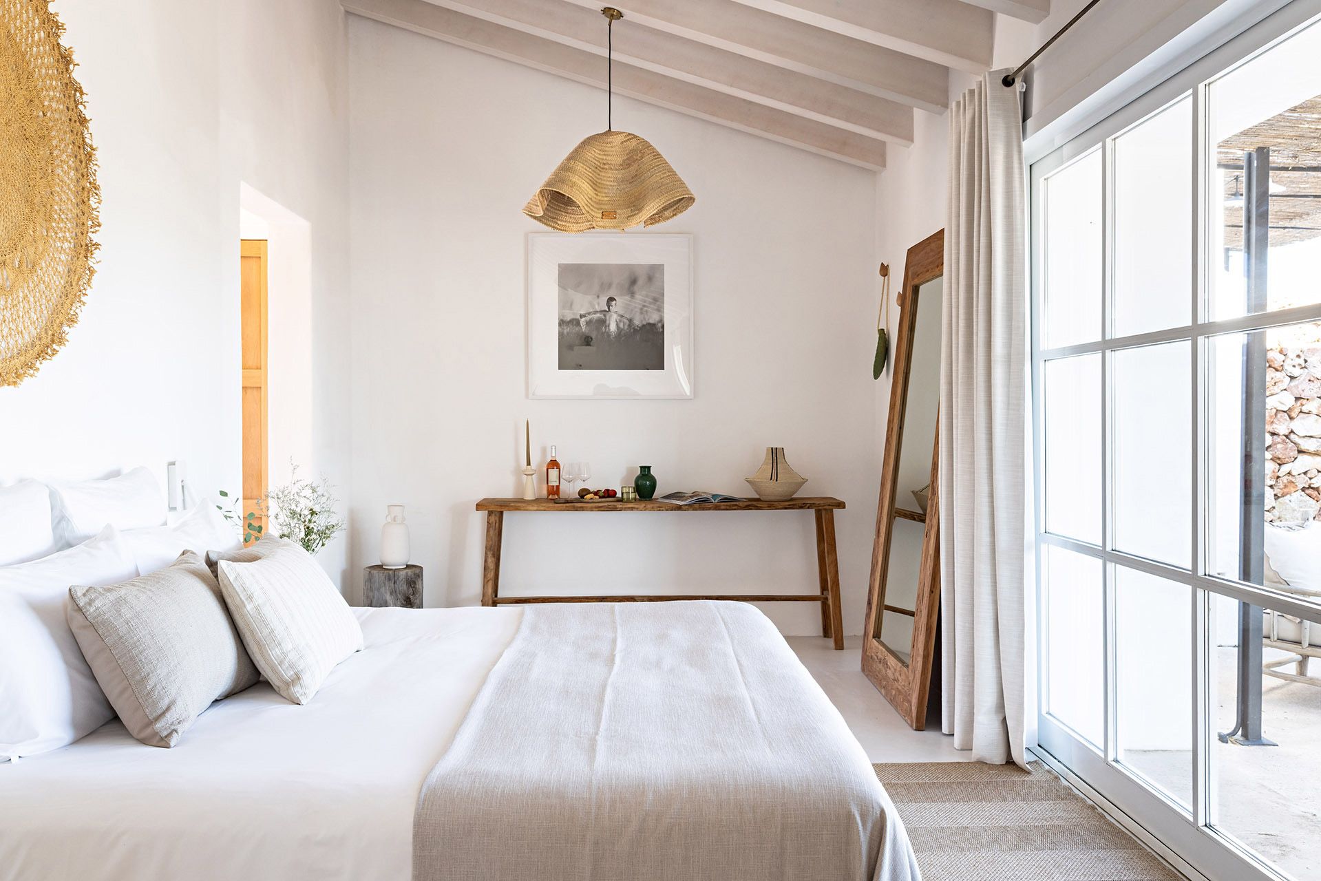 Un dormitorio con cama, mesita de noche y un ventanal grande.