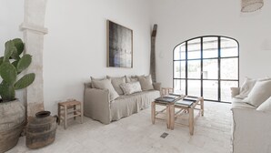 A minimalist living room with a large arched window, a sofa, a coffee table, and a cactus plant. - Torre Vella – Fontenille Collection (Alayor)