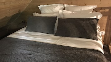 A cozy loft bedroom with a sloped ceiling, wooden walls, and a bed with white and dark gray bedding.