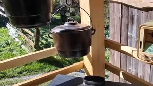 Une cuisinière portative dotée de quatre brûleurs et d’un évier, installée sur une terrasse en bois où sont suspendues des casseroles.