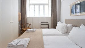 Ett hotellrum med en säng, en stol, en garderob, ett fönster och en inramad tavla på väggen.