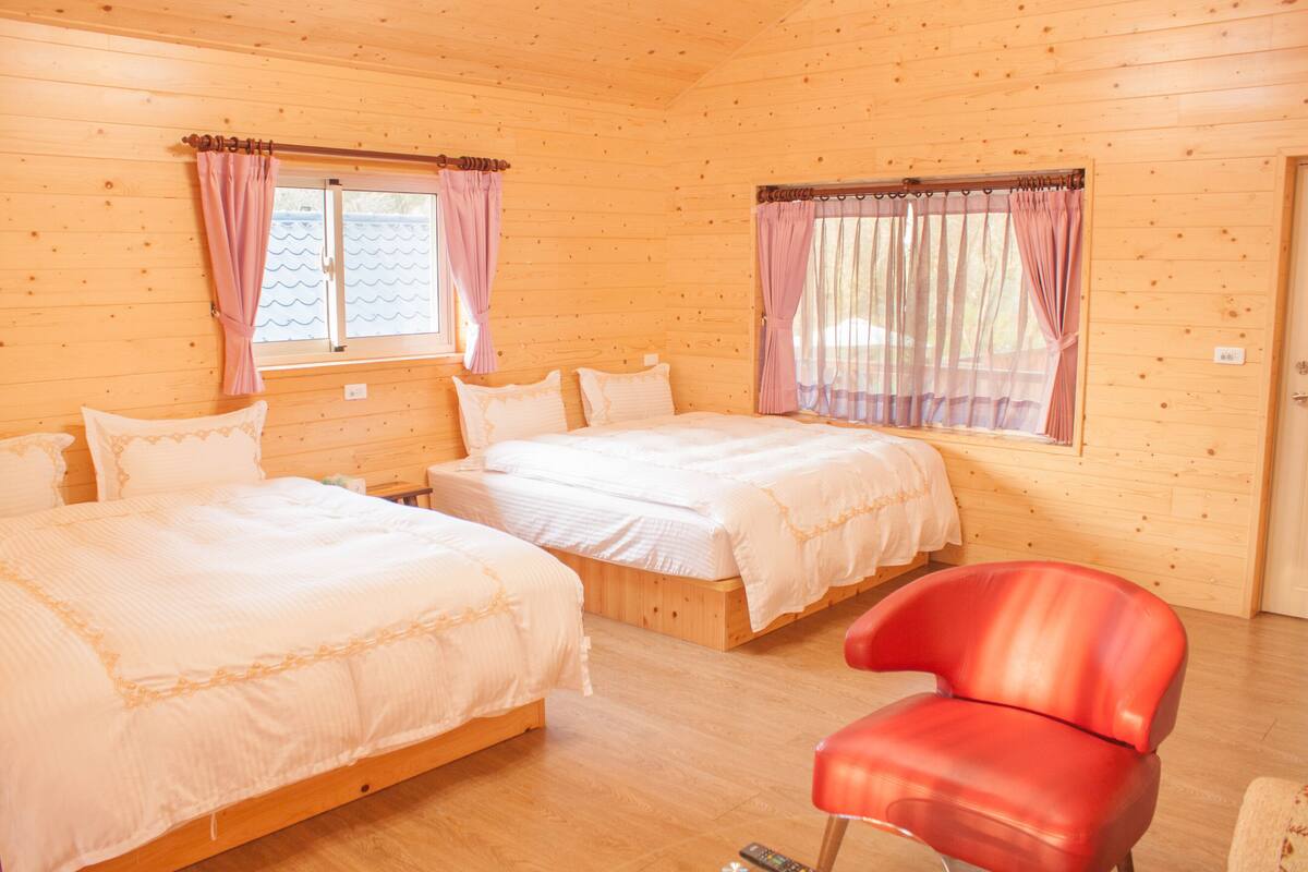 Una cabaña de madera con dos camas, una silla roja y una ventana con cortinas.