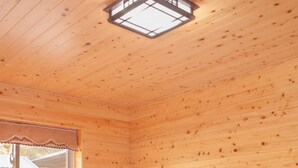 A wooden cabin room with two beds, a window with a curtain, and a skylight.