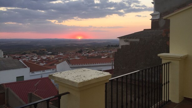 Un balcón con vistas a una puesta de sol sobre un pueblo de tejados rojos.