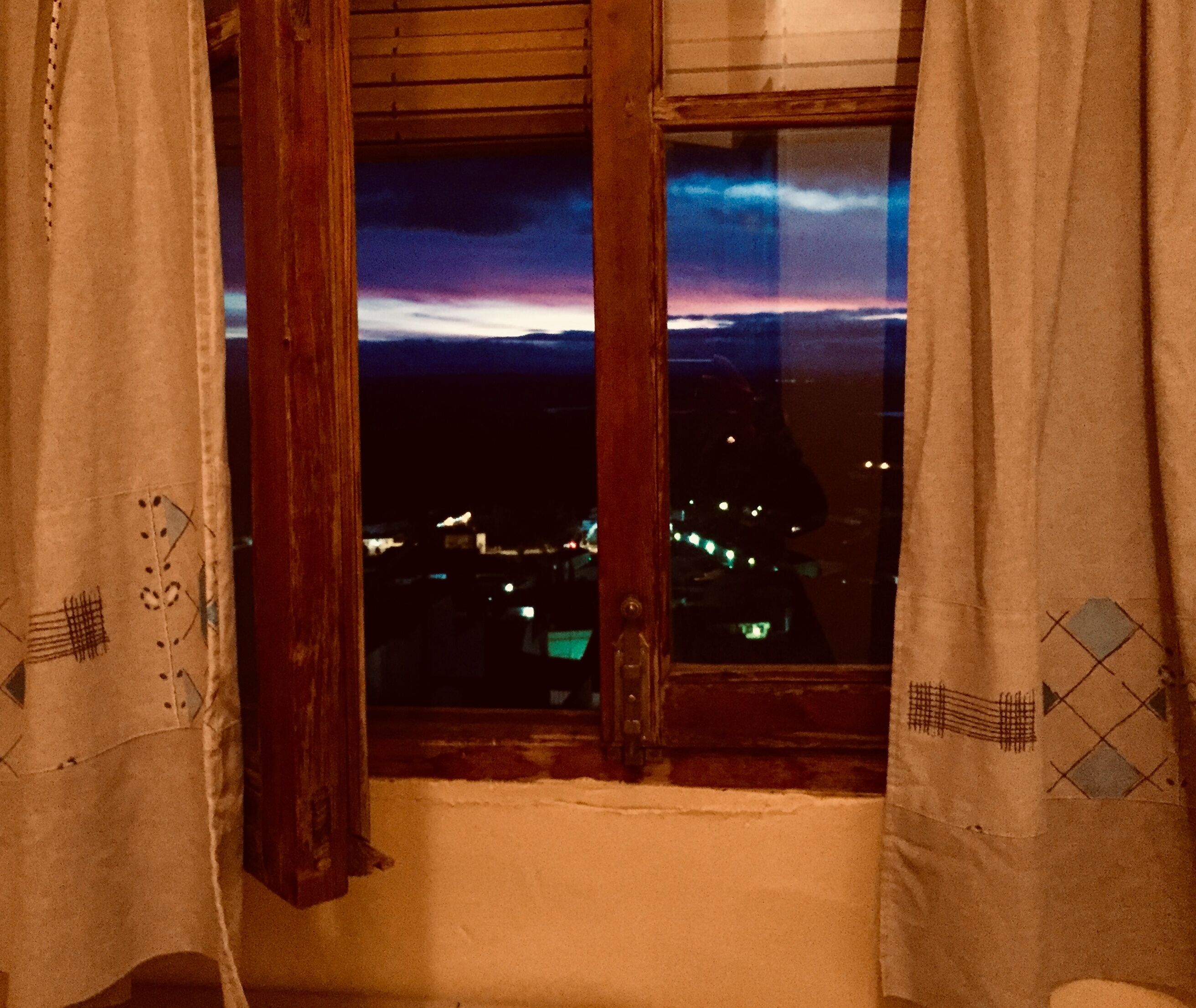 A room with a view of a cityscape at dusk through an open window.