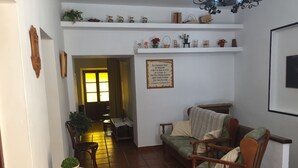 Una sala de estar con un sofá, sillas, una mesa y una planta en maceta. Hay un cartel en la pared y una ventana con cortinas.