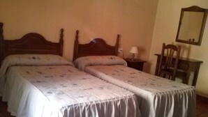 Una habitación con dos camas individuales, una mesita, una silla y un espejo en la pared.