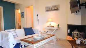 A living room with a white sofa, a glass coffee table, a fireplace, and a television mounted on the wall. - Areos Galaxy Apartments With Beach View (Spata-Artemida)