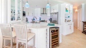 A modern kitchen with white cabinetry, a central island with seating, stainless steel appliances, and a wine cooler. - Beachfront 2-bed Apt with two pools - Sapphire 401 (Dover)
