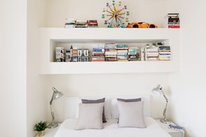 A neatly organized bedroom with a bed, two bedside lamps, a small plant, and a bookshelf with books and a toy car.