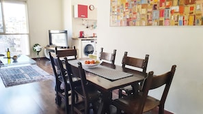 Uma sala de jantar com uma mesa de madeira, seis cadeiras, uma tigela de frutas e uma televisão.