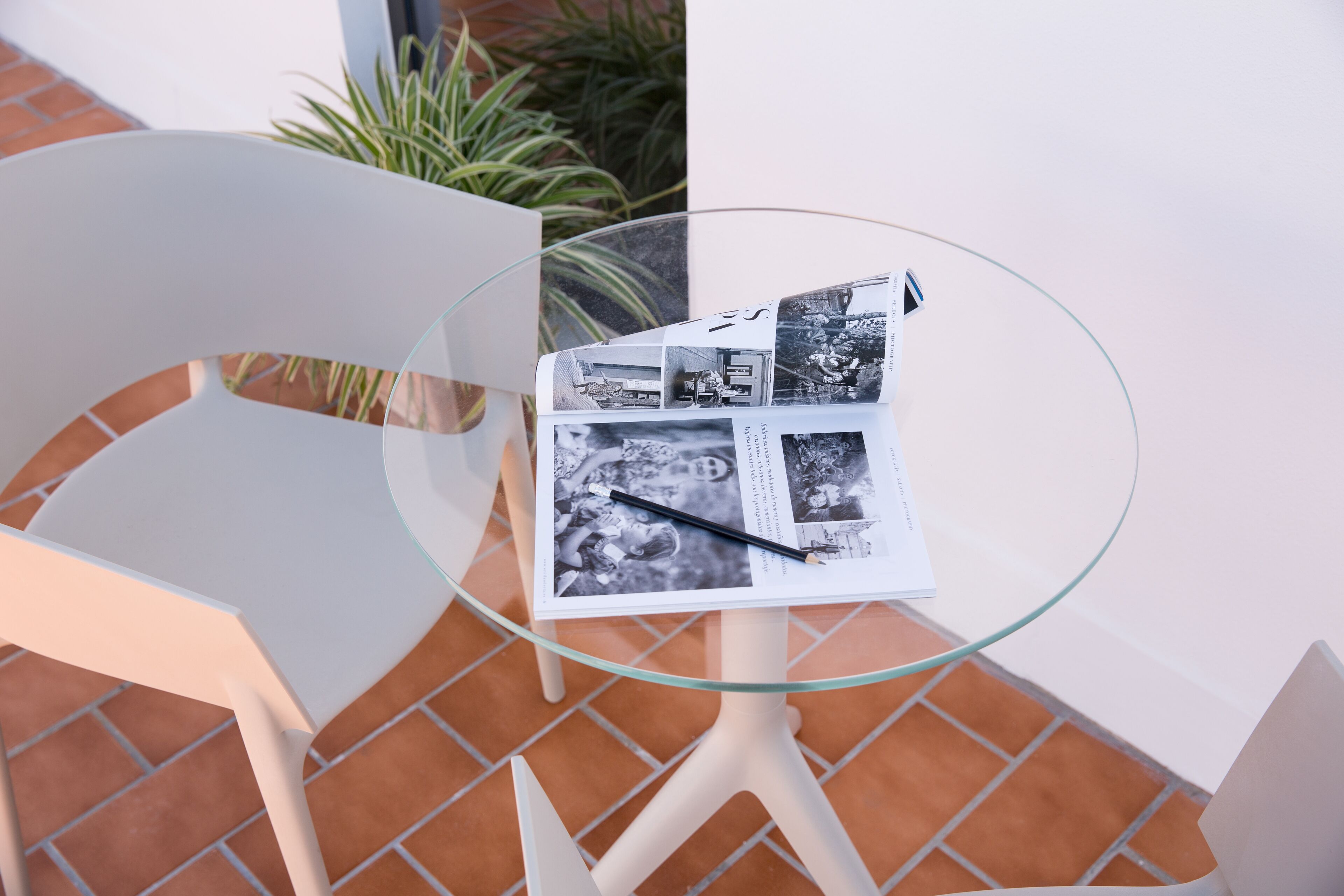 Een glazen tafel met een tijdschrift en een pen, omringd door witte stoelen.