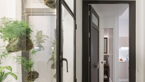 Un interior moderno con un vidrio que da a un balcón, un pasillo con una cocina visible a través de una puerta abierta.