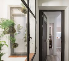 A modern interior with a glass door leading to a balcony, a hallway with a kitchen area visible through an open door.