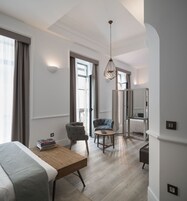 A modern hotel room with a wooden bed, a desk, a chair, a small table, and a hanging light fixture.