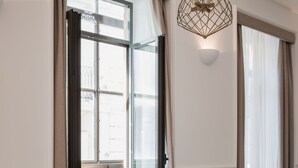 Una habitación amplia con ventanas grandes, dos sillones tapizados, una pequeña mesa de madera y una lámpara colgante.