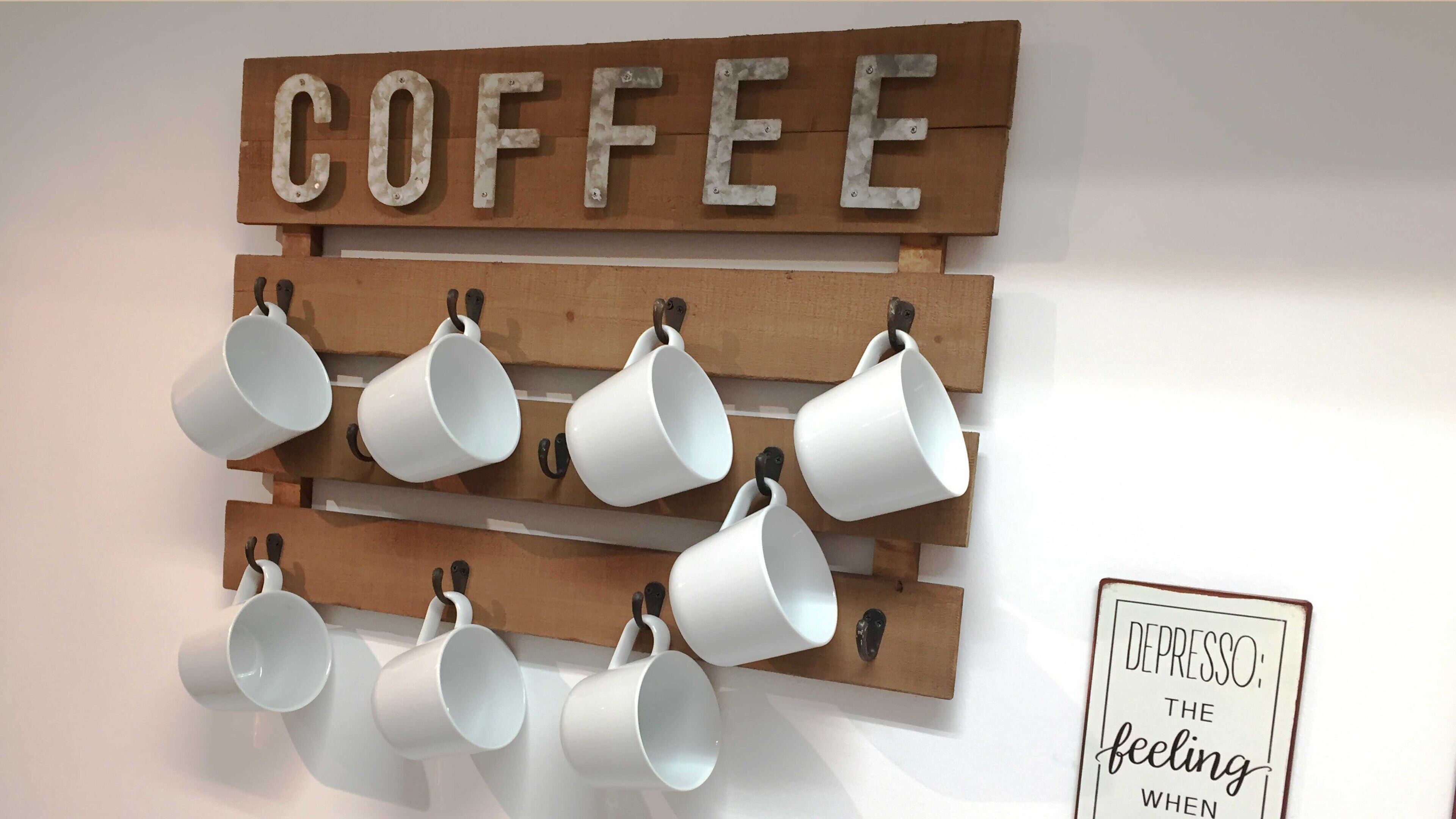 A wall-mounted coffee rack with multiple white mugs and a sign above it that reads "COFFEE".