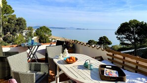 A balcony with wicker furniture, a table with a bowl of fruit, a teapot, and a basket of magazines.