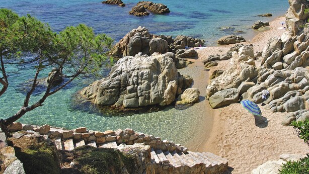 A rocky beach with clear water, a stone wall, and a beach umbrella.