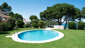 A swimming pool surrounded by well-maintained grass and trees, with a clear blue sky above.