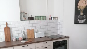 Een kleine keuken met witte kasten, een houten aanrecht, een rode stoel en een betegelde spatwand.