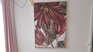 Een woonkamer met een rode fluweelzofa, een ronde salontafel en een groot bloemschilderij aan de muur.