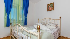 A bed with a metal frame, white bedding, and a blue curtain. - Apartment Dadi (Crikvenica)