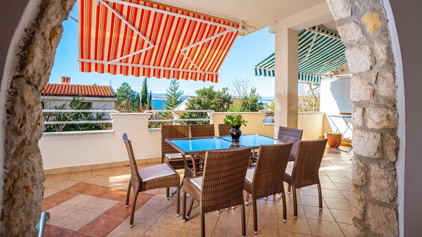 A terrace with a table and chairs, a potted plant, and striped awnings. - Apartment Dadi (Crikvenica)